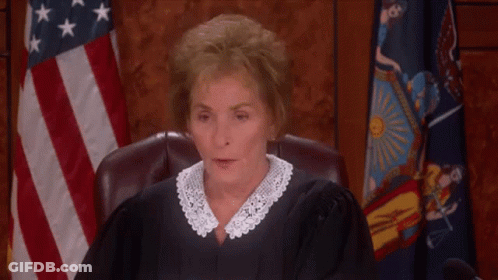 A Female Judge Is Sitting In A Courtroom With Her Eyes Closed And A Flag In The Background . GIF
