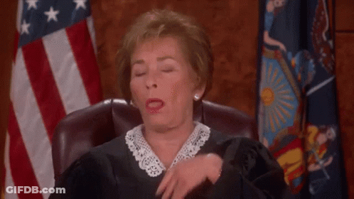 A Female Judge Is Sitting In A Courtroom With Her Eyes Closed And A Flag In The Background . GIF