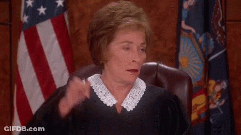 A Female Judge Is Sitting In Front Of An American Flag And Scratching Her Head . GIF