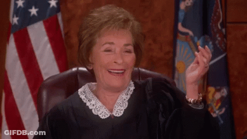 A Female Judge Is Smiling While Sitting In A Courtroom In Front Of An American Flag . GIF