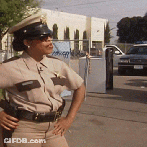 A Female Police Officer Stands In Front Of A Building That Has The Word Houses On It GIF