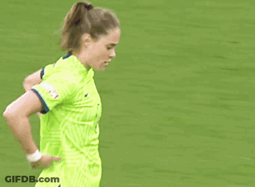 A Female Soccer Player In A Neon Green Jersey Is Standing On The Field . GIF