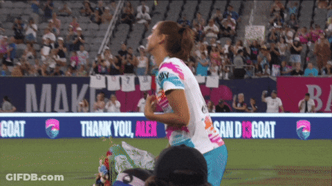 A Female Soccer Player Stands On The Field In Front Of A Banner That Says " Thank You Men " GIF