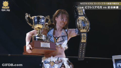 A Female Wrestler Holding A Trophy And A Belt That Says Victoria GIF