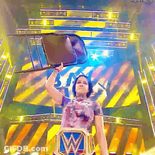 A Female Wrestler Holds A Chair Over Her Head While Wearing A W Belt GIF