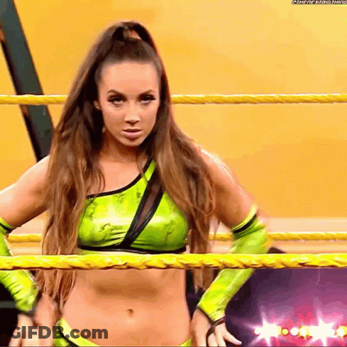A Female Wrestler In A Green Outfit Is Standing In A Ring GIF