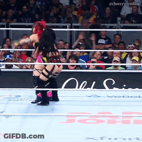 A Female Wrestler Is Being Lifted In The Air By Another Wrestler In A Wrestling Ring GIF