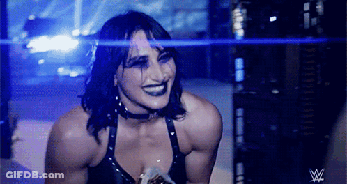 A Female Wrestler Is Smiling In Front Of A W Logo GIF