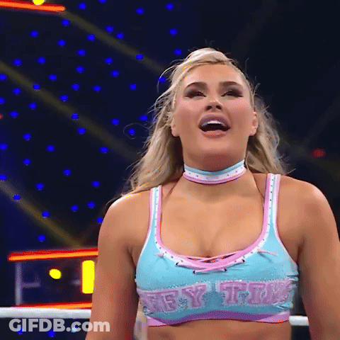 A Female Wrestler Is Standing In A Ring Wearing A Blue And Pink Top And Choker . GIF