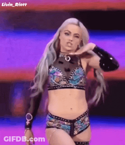 A Female Wrestler Is Standing On A Stage In A Purple And Blue Outfit . GIF