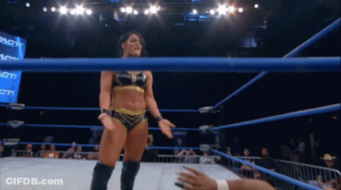 A Female Wrestler Stands In A Wrestling Ring With A Crowd Behind Her GIF