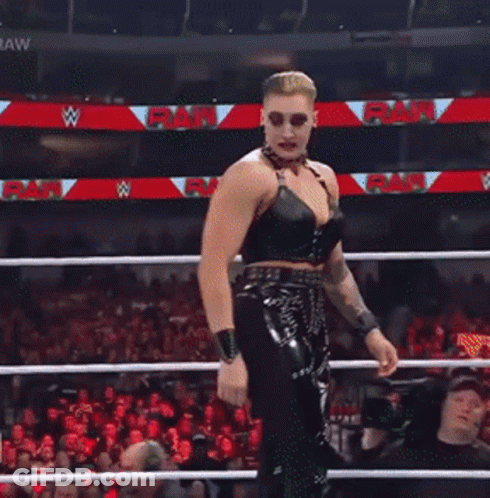 A Female Wrestler Stands In A Wrestling Ring With A Crowd Watching And A Sign That Says Raw GIF