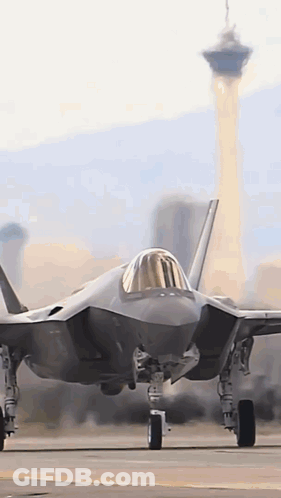 A Fighter Jet Is Sitting On A Runway With A City In The Background . GIF