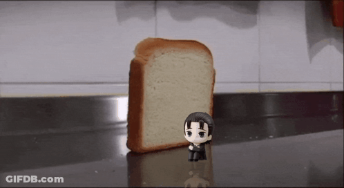 A Figurine Of A Man Is Standing Next To A Slice Of Bread . GIF
