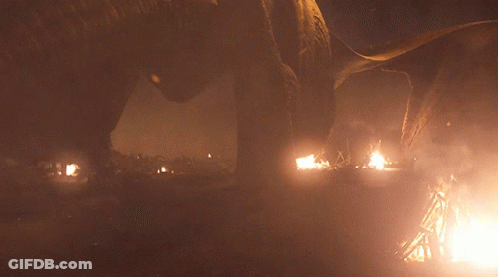A Fire Is Burning In A Dark Area With A Few Buildings In The Background GIF