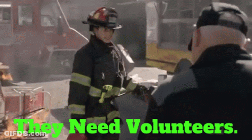 A Firefighter Talking To Another Firefighter With The Words " They Need Volunteers " Behind Her GIF