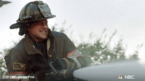 A Fireman Wearing A Helmet And A Rescue Squad Armband Is Spraying Water GIF