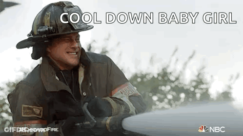 A Fireman Wearing A Helmet Is Spraying Water From A Hose . GIF
