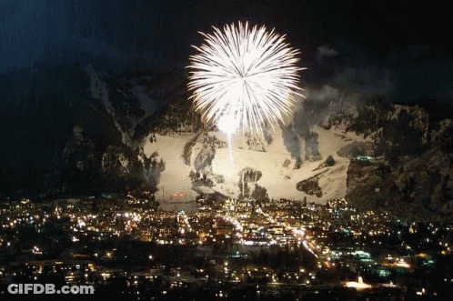 A Fireworks Display In Front Of A Snowy Mountain Over A City GIF