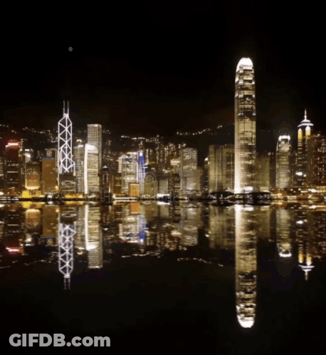 A Fireworks Display Over A City With A Reflection In The Water GIF