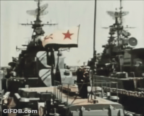 A Flag With A Red Star On It Is Flying In Front Of A Military Ship GIF