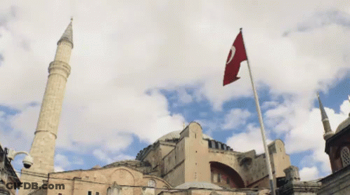 A Flag With The Letter C On It Is Flying In Front Of A Large Building GIF