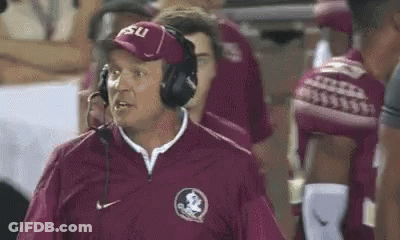 A Football Coach Wearing Headphones And A Hat Is Standing On The Sidelines . GIF