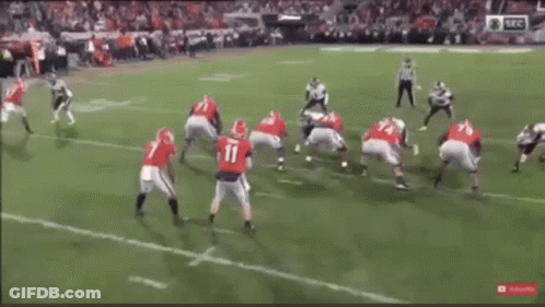 A Football Game Is Being Played On A Field With A Referee In The Background . GIF