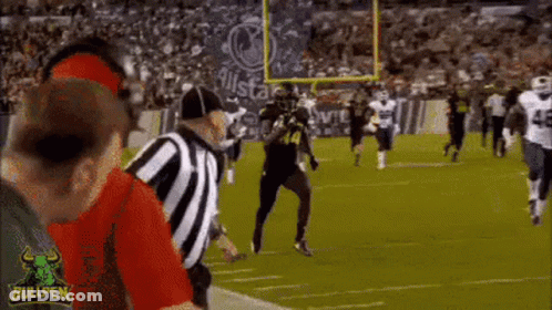 A Football Game Is Being Played On A Field With A Referee Standing In The Middle . GIF