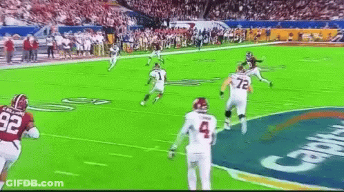 A Football Game Is Being Played On A Green Field With A Crowd In The Background . GIF