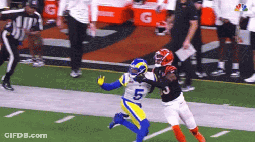 A Football Player In A Blue And Yellow Uniform Is Trying To Catch A Pass From Another Player In A Black Uniform . GIF