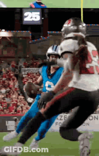 A Football Player In A Blue Jersey Is Being Tackled By Another Player On The Field . GIF