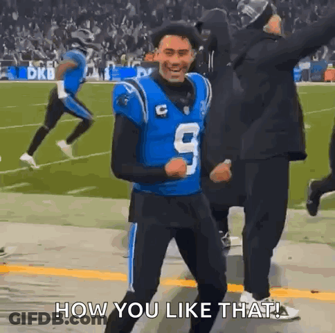 A Football Player In A Blue Jersey Is Dancing On The Field While A Crowd Watches . GIF