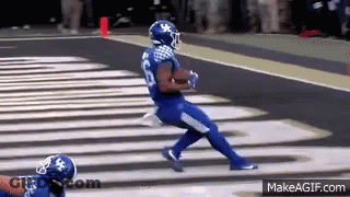 A Football Player In A Blue Jersey Is Running Down The Field . GIF