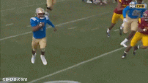 A Football Player In A Blue Jersey Is Running With A Ball On A Field . GIF