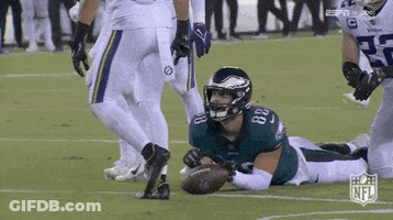 A Football Player In A Green Uniform Is Laying On The Field With A Ball . GIF