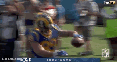 A Football Player In A Rams Jersey Is Holding A Football In His Hands . GIF