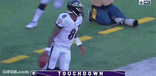 A Football Player In A Ravens Uniform Is Holding A Football In Front Of A Touchdown Screen GIF
