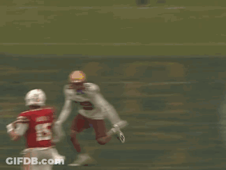 A Football Player In A Red Jersey And White Pants Is Being Tackled By Another Player On The Field . GIF