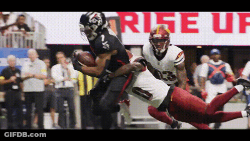 A Football Player In A Red Uniform Is Being Tackled By Another Player In A Black Uniform GIF