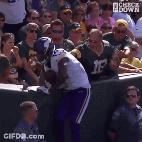 A Football Player Is Being Tackled By A Fan While A Crowd Watches . GIF