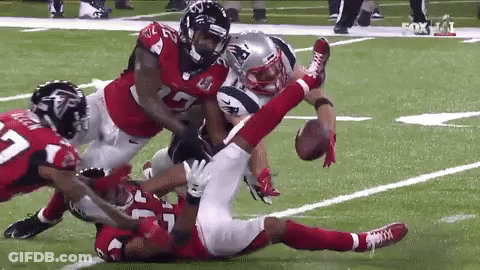 A Football Player Is Being Tackled By A Group Of Players On A Field . GIF