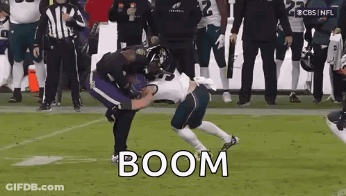 A Football Player Is Being Tackled By Another Player On A Field While A Referee Watches . GIF