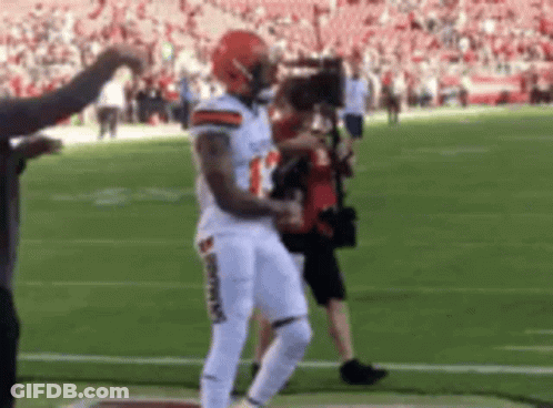 A Football Player Is Dancing On The Field While A Cameraman Takes A Picture . GIF