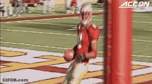 A Football Player Is Holding A Ball In Front Of A Red Pole That Says Accon On It GIF