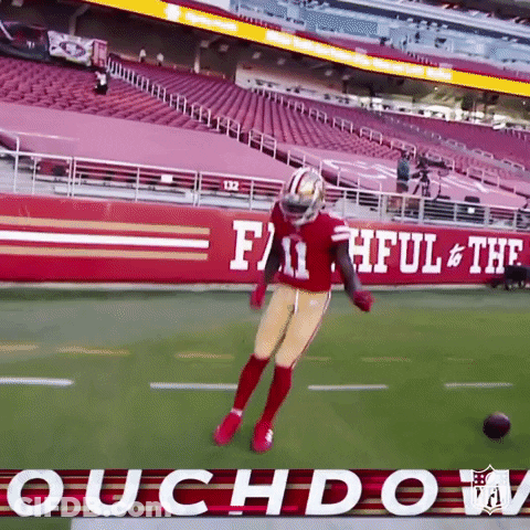 A Football Player Is Jumping In The Air On A Field In Front Of A Sign That Says Faithful & The Roughdown GIF