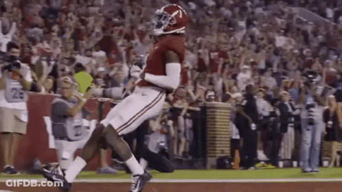 A Football Player Is Jumping In The Air While Catching A Pass On A Field . GIF