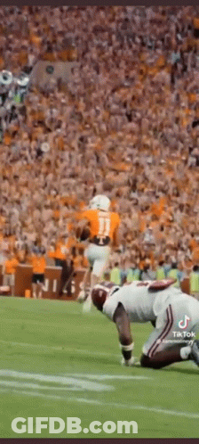 A Football Player Is Kneeling On The Field In Front Of A Crowd While Another Player Runs With The Ball . GIF