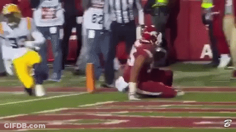 A Football Player Is Kneeling On The Field While A Referee Looks On GIF
