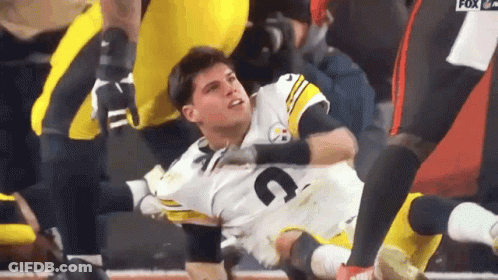 A Football Player Is Laying On The Ground While Being Helped By A Teammate . GIF